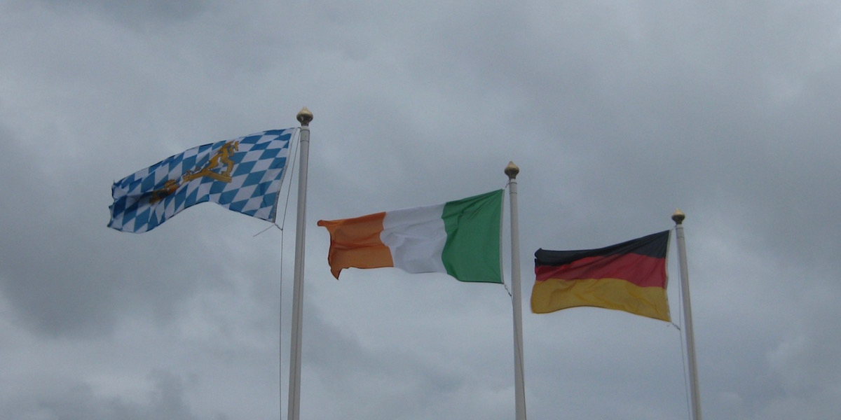 Die bayrische, irische und deutsche Flagge vor einem bewölkten Himmel