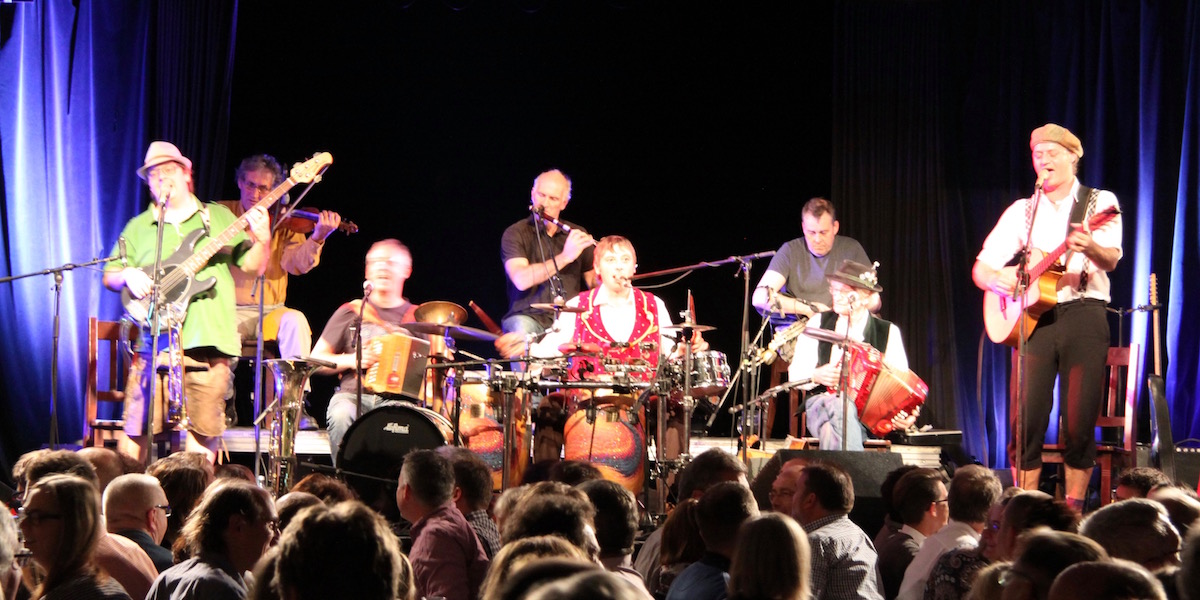 The eight musicians of Da Huawa, da Meier und I and Na Ciotogi are standing and sitting on the stage playing an Irish-Bayrisch song