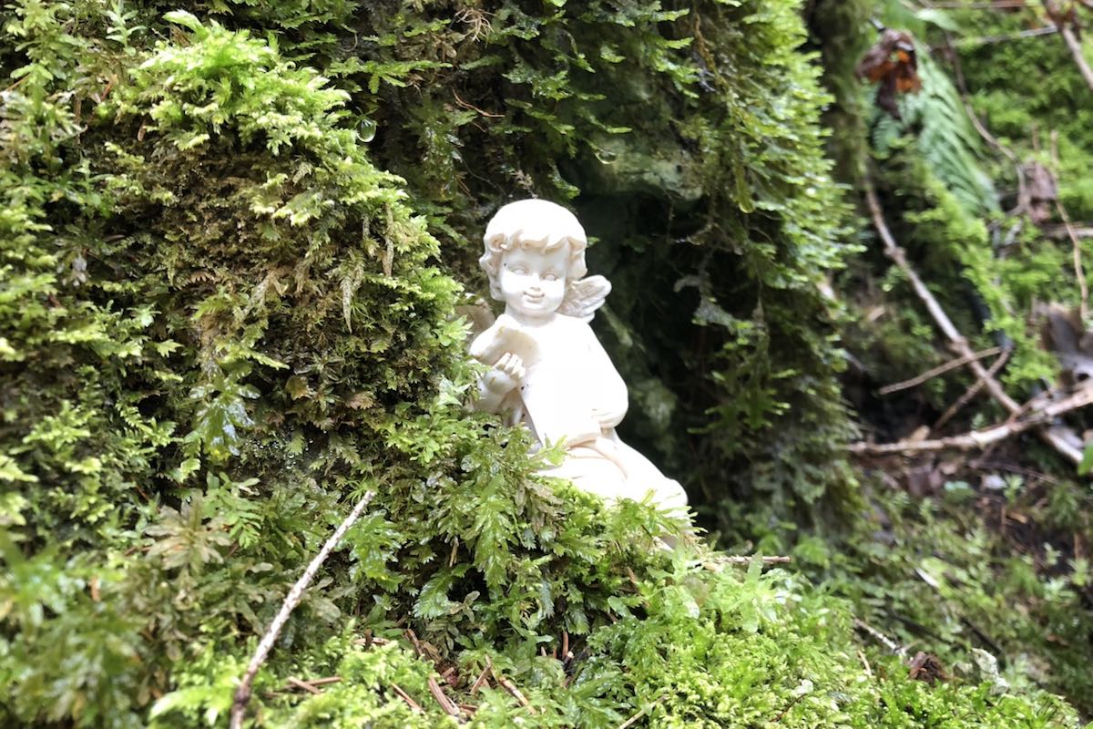 White figure of an angel sitting in an area overgrown with moss